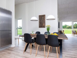 A modern kitchen with a large island, black chairs, white pendant lights, and a view of the outdoors. - 4 Star Holiday Home in Ansager (Ansager)