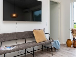 Ein modernes Wohnzimmer mit einem großen Flachbildfernseher an der Wand, einem grauen Sofa mit einem braunen Kissen und einem Korbwäschekorb auf dem Boden.