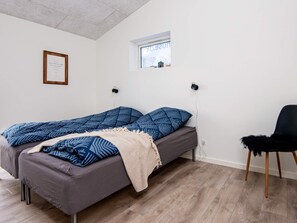 A single bed with a patterned blanket, a small window, and a chair.