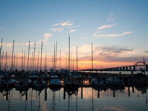 A marina with multiple boats docked at the pier, reflecting on the water during sunset.