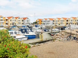 A marina with boats docked, a wooden pier, and a row of buildings with red roofs.