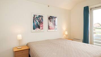 A bedroom with a bed, bedside tables, and two wall-mounted paintings.