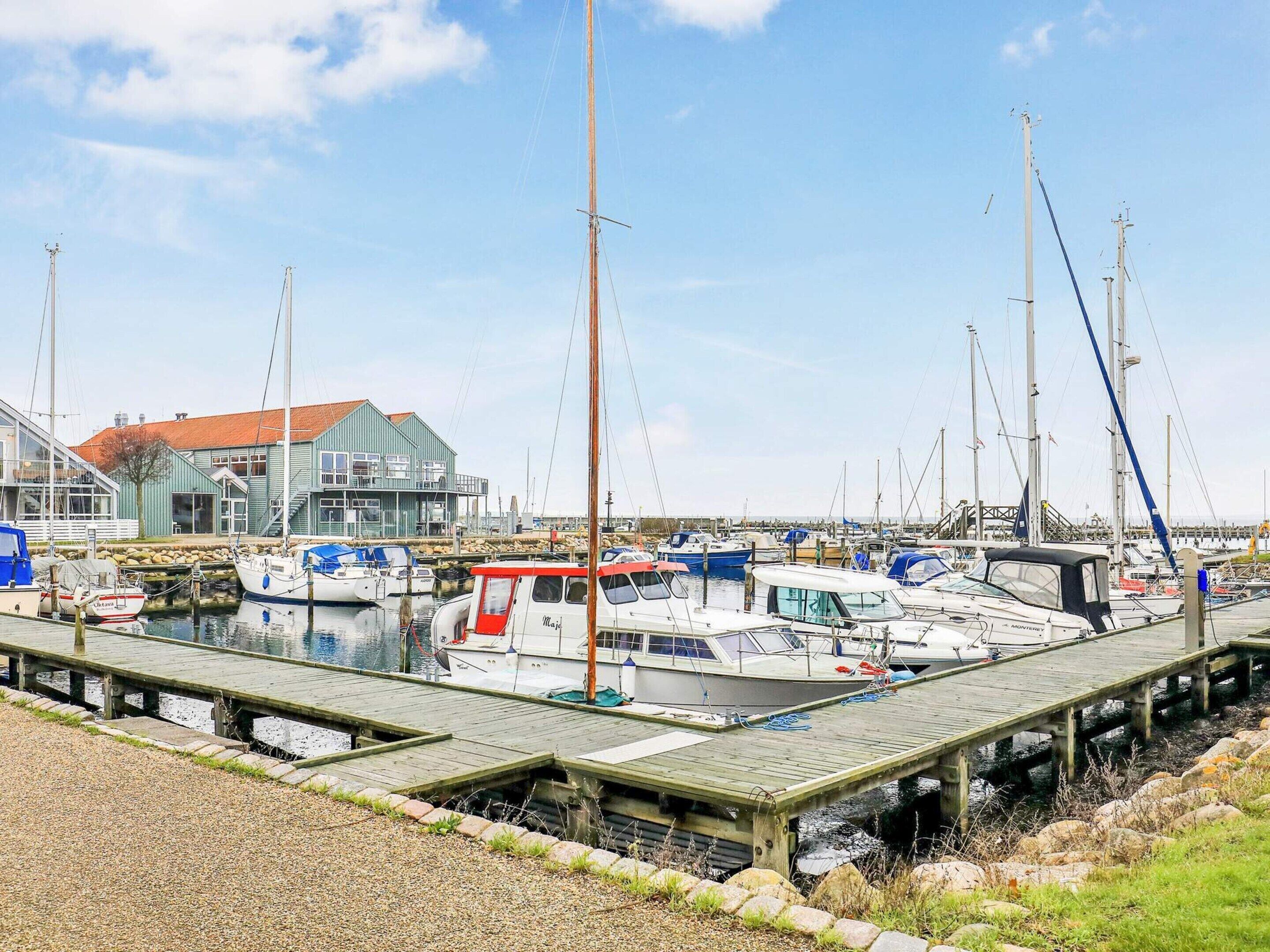 Een jachthaven met meerdere boten die aanmeren, een houten steiger en een gebouw met een rood dak op de achtergrond.
