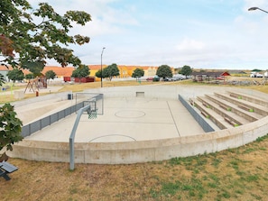 A basketball court with a basketball hoop, a bench, and a playground area. - 4 Star Holiday Home in Rudkobing (Rudkobing)