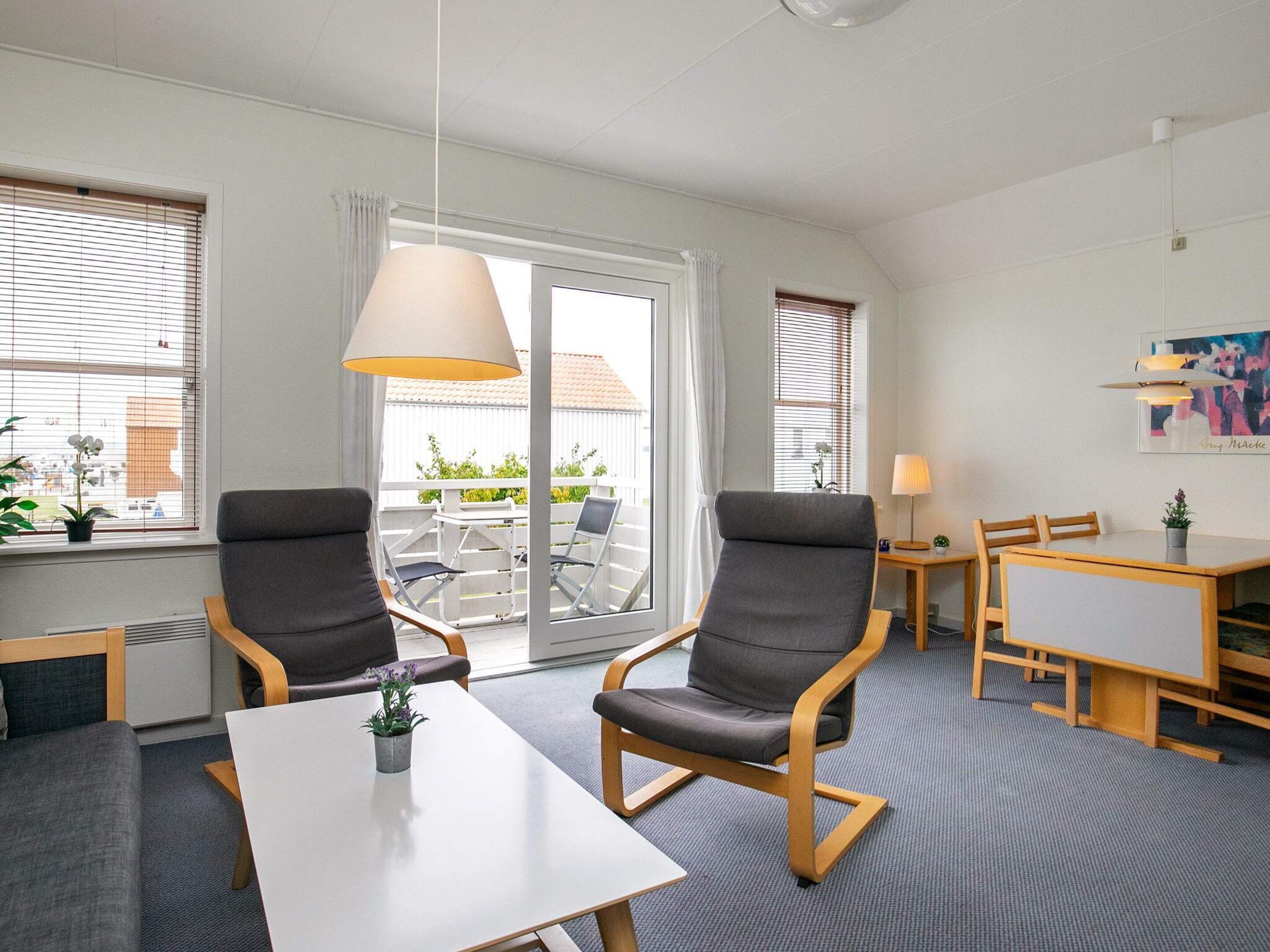A hotel room with a balcony, two armchairs, a dining table, and a lamp.