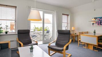 A hotel room with a balcony, two armchairs, a dining table, and a lamp.