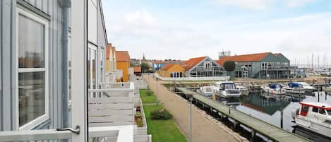 A marina with boats docked, a grassy area, and buildings with red roofs in the background.