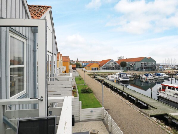 A marina with boats docked, a grassy area, and buildings with red roofs in the background.