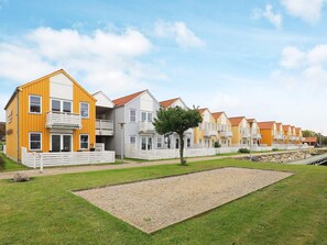 A row of modern, multi-story residential buildings with balconies, set in a grassy area with a gravel path.
