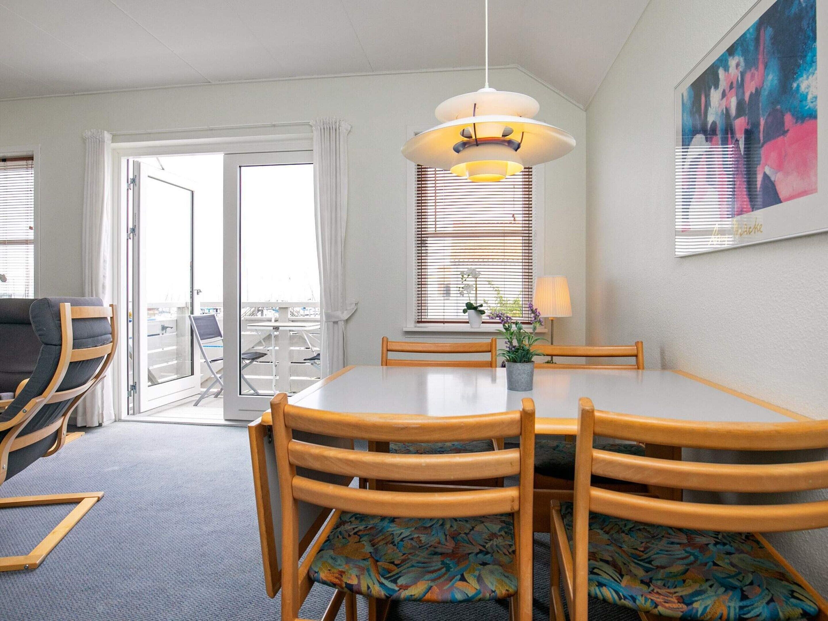 A dining area with a round table, wooden chairs, a hanging light fixture, and a window with blinds.