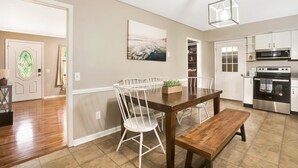 A modern kitchen with white cabinetry, stainless steel appliances, and a wooden dining table with chairs. - Country Lane Cottage, Privacy & Quiet Neighborhood (Rossville)