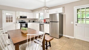A modern kitchen with white cabinets, stainless steel appliances, and a wooden dining table. - Country Lane Cottage, Privacy & Quiet Neighborhood (Rossville)