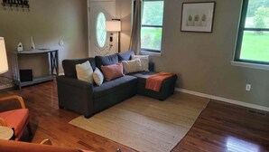 A living room with a sectional sofa, a small table, a rug, and a door with a frosted glass window. - Country Lane Cottage, Privacy & Quiet Neighborhood (Rossville)