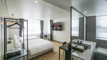 A modern hotel room with a large bed, a desk, a mirror, and a TV mounted on the wall.