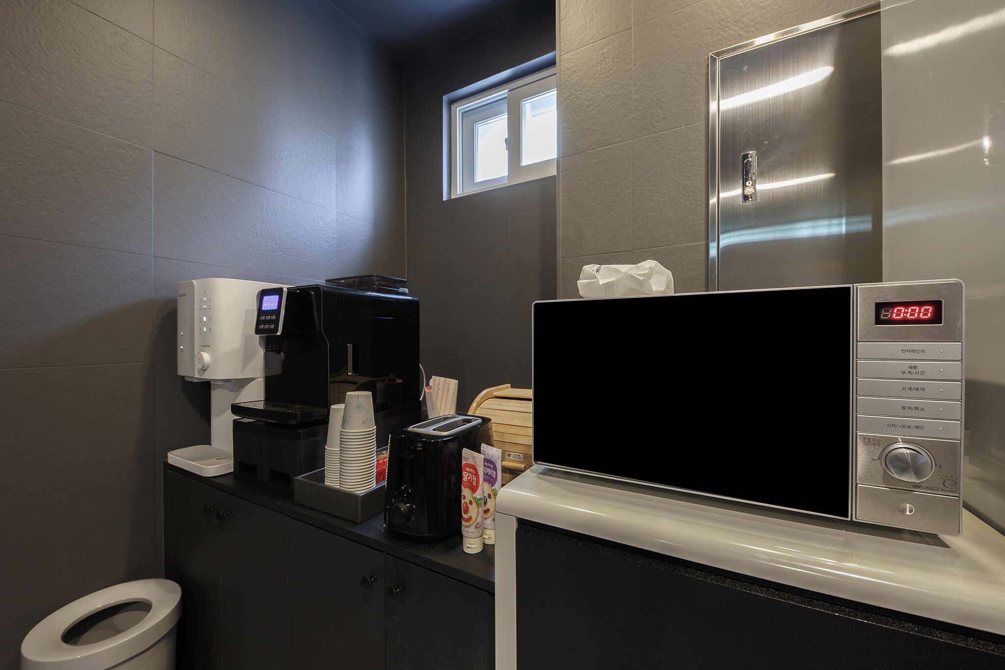 A modern bathroom with a coffee machine, microwave, and a digital clock displaying 8:38.