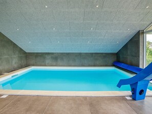 A modern indoor swimming pool with a blue slide, tiled walls, and a sloped ceiling. - 22 Person Holiday Home in Vaeggerlose (Vaeggerlose)