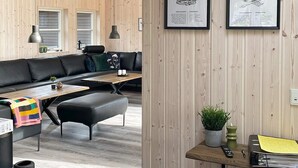 En moderne stue med en sort lædersofa, et træsofabord og en sort bænk. Der er en lille plante på et træsidebord, og en rammet menu hænger på væggen.
