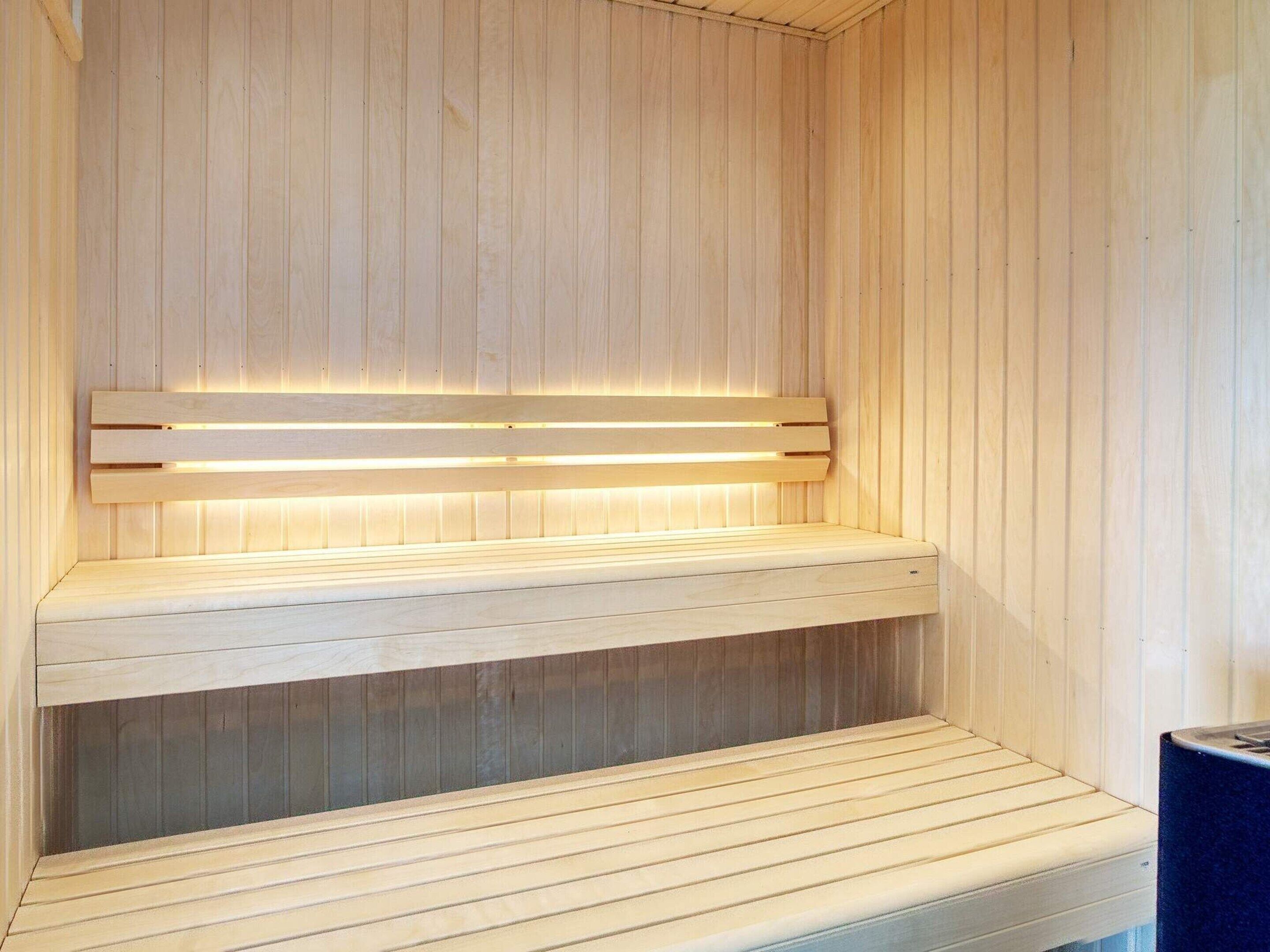 Un sauna avec des bancs en bois et un banc doté d’un dossier éclairé.