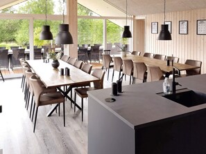 Un comedor amplio con largas mesas de madera y sillas modernas, ventanas grandes y lámparas colgantes.
