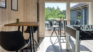 Et værelse med trævæg, et bord med stole, et bordtennisbord og et vindue med udsigt til grøn natur.
