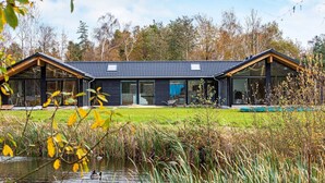 Et moderne hus i to etager med store glasvinduer, et tegltag og en græsplænde.