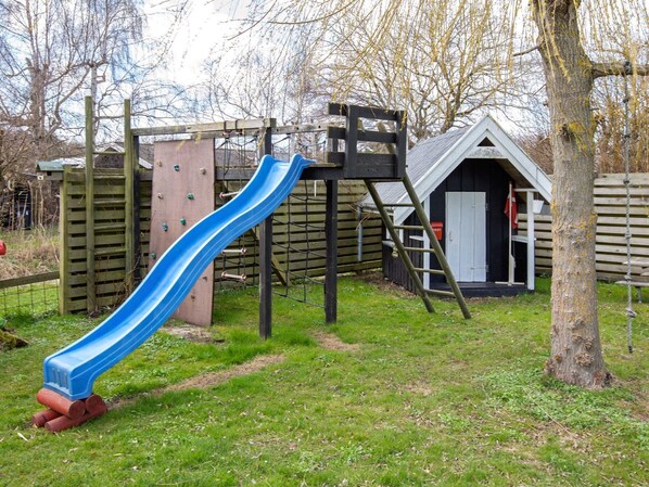 A playground with a blue slide, climbing structures, and a small building with a door.