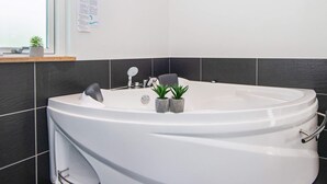 A modern bathroom with a large freestanding bathtub, a small sink, and a window providing natural light. - 4 Star Holiday Home in Silkeborg (Silkeborg)
