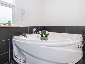 A modern bathroom with a large freestanding bathtub, a small sink, and a window providing natural light. - 4 Star Holiday Home in Silkeborg (Silkeborg)