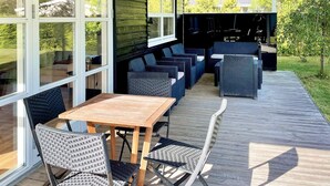 An outdoor patio with a wooden table and chairs, a covered seating area with sofas and chairs, and large windows offering views of the surrounding greenery. - 4 Star Holiday Home in Silkeborg (Silkeborg)