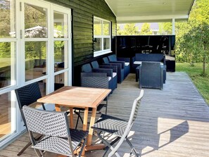 An outdoor patio with a wooden table and chairs, a covered seating area with sofas and chairs, and large windows offering views of the surrounding greenery. - 4 Star Holiday Home in Silkeborg (Silkeborg)