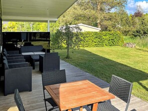 An outdoor patio with a wooden table and chairs, surrounded by a covered seating area with sofas and a dining table. - 4 Star Holiday Home in Silkeborg (Silkeborg)