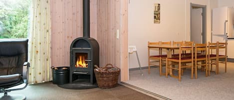 A room with a wood-burning stove, a dining table with chairs, and a window with curtains.