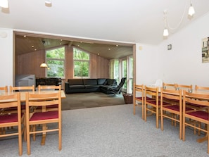 A room with a wooden floor, a black sofa, a dining table with chairs, and large windows.