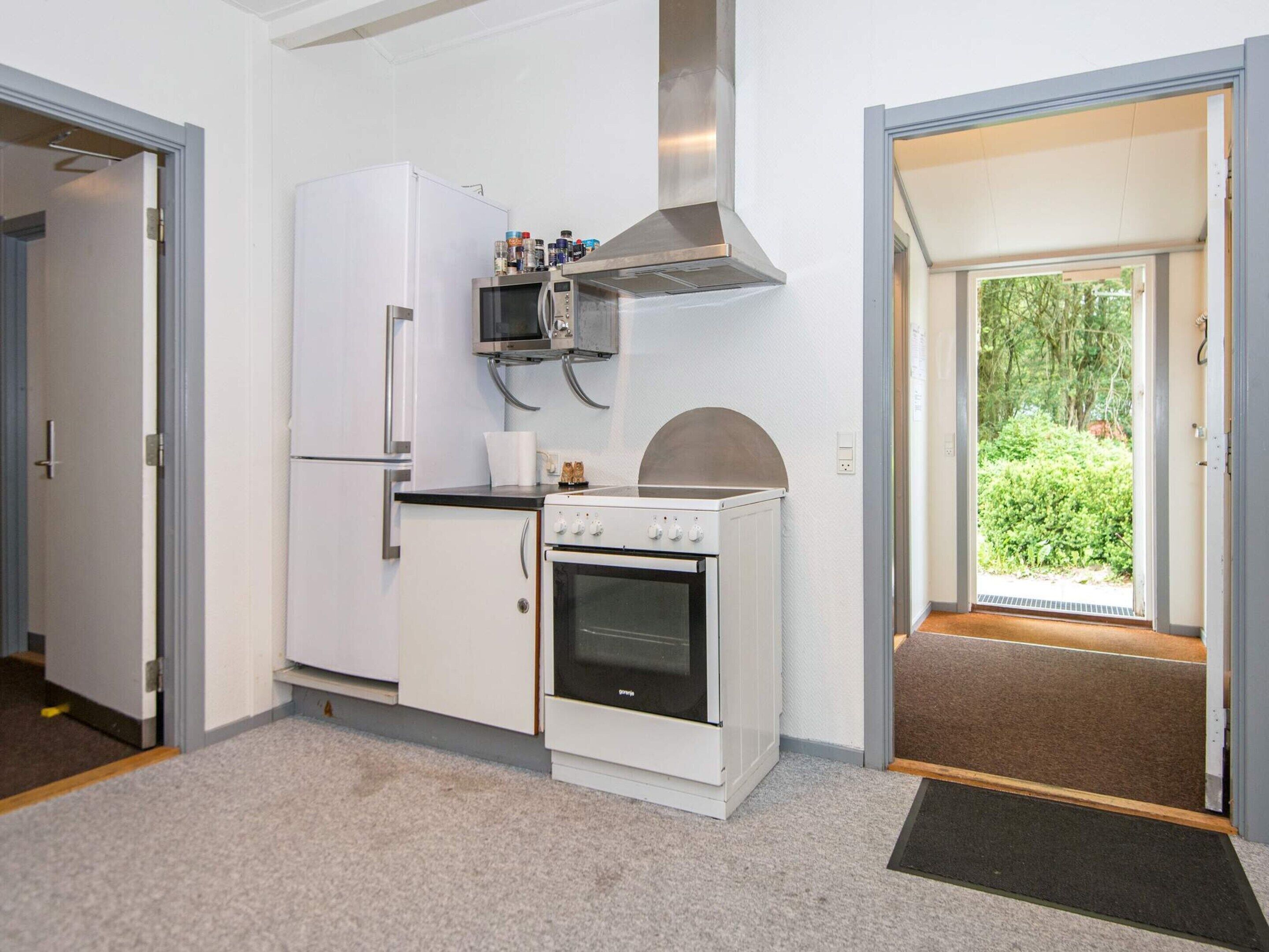A compact kitchen with a refrigerator, microwave, stove, and a small window.