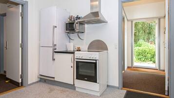 A compact kitchen with a refrigerator, microwave, stove, and a small window.