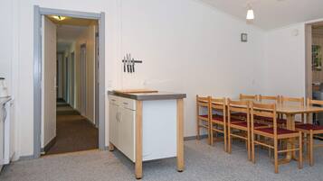 A compact kitchen with a dining area, featuring a central island with a cutting board, a set of knives on the wall, and a table with chairs.