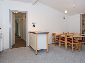 Et kompakt køkken med spiseplads, med en central ø med skærebræt, en knivsamling på væggen og et bord med stole.