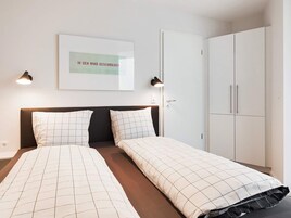 Et hotelværelse med en seng, to sengeborde med lamper, et klædeskab og et billede i ramme på væggen.