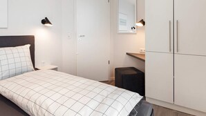 A bedroom with a bed, a wardrobe, a desk, and a mirror.