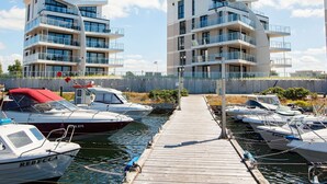 A marina with modern apartment buildings, boats docked, and a wooden walkway.