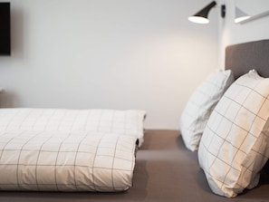 A neatly made bed with a checkered bedspread and two pillows, a bedside lamp, and a wall-mounted light fixture.