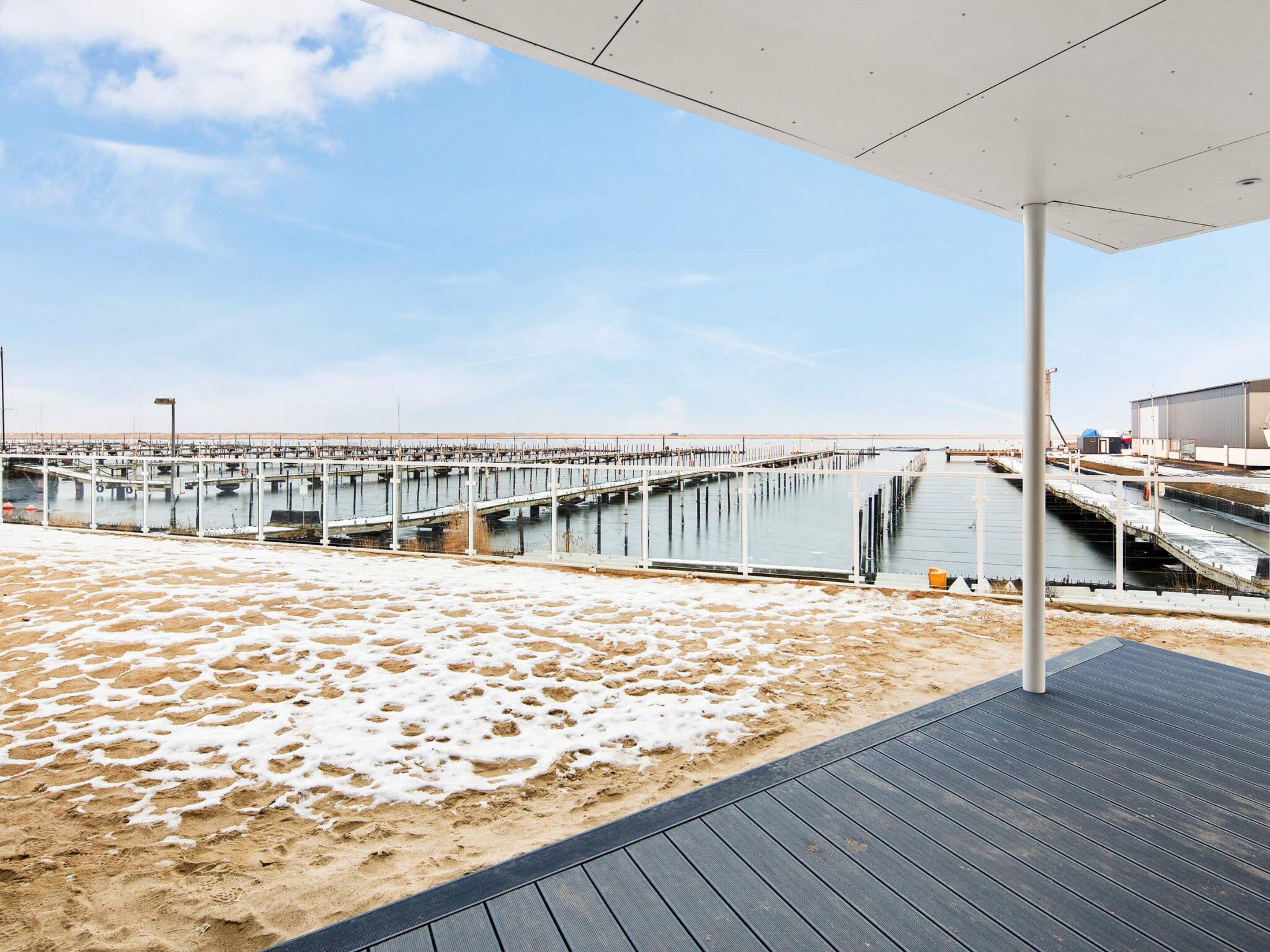 A beach with a pier extending into the water, a covered area with a roof, and a sandy area with footprints.