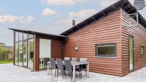 A modern house with a wooden exterior, large glass windows, and a patio with a table and chairs. - 4 Star Holiday Home in Vestervig (Vestervig)