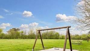 A wooden swing set in a grassy park area with a bench and trees in the background.