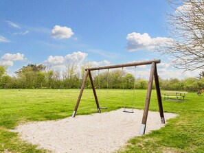 A wooden swing set in a grassy park area with a bench and trees in the background. - 4 Star Holiday Home in Vestervig (Vestervig)