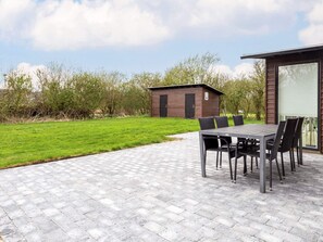 An outdoor patio with a table and chairs, a small shed, and a grassy area with trees. - 4 Star Holiday Home in Vestervig (Vestervig)