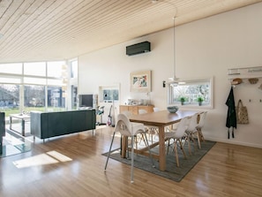 A modern kitchen with a wooden dining table, white chairs, and a large window providing natural light.