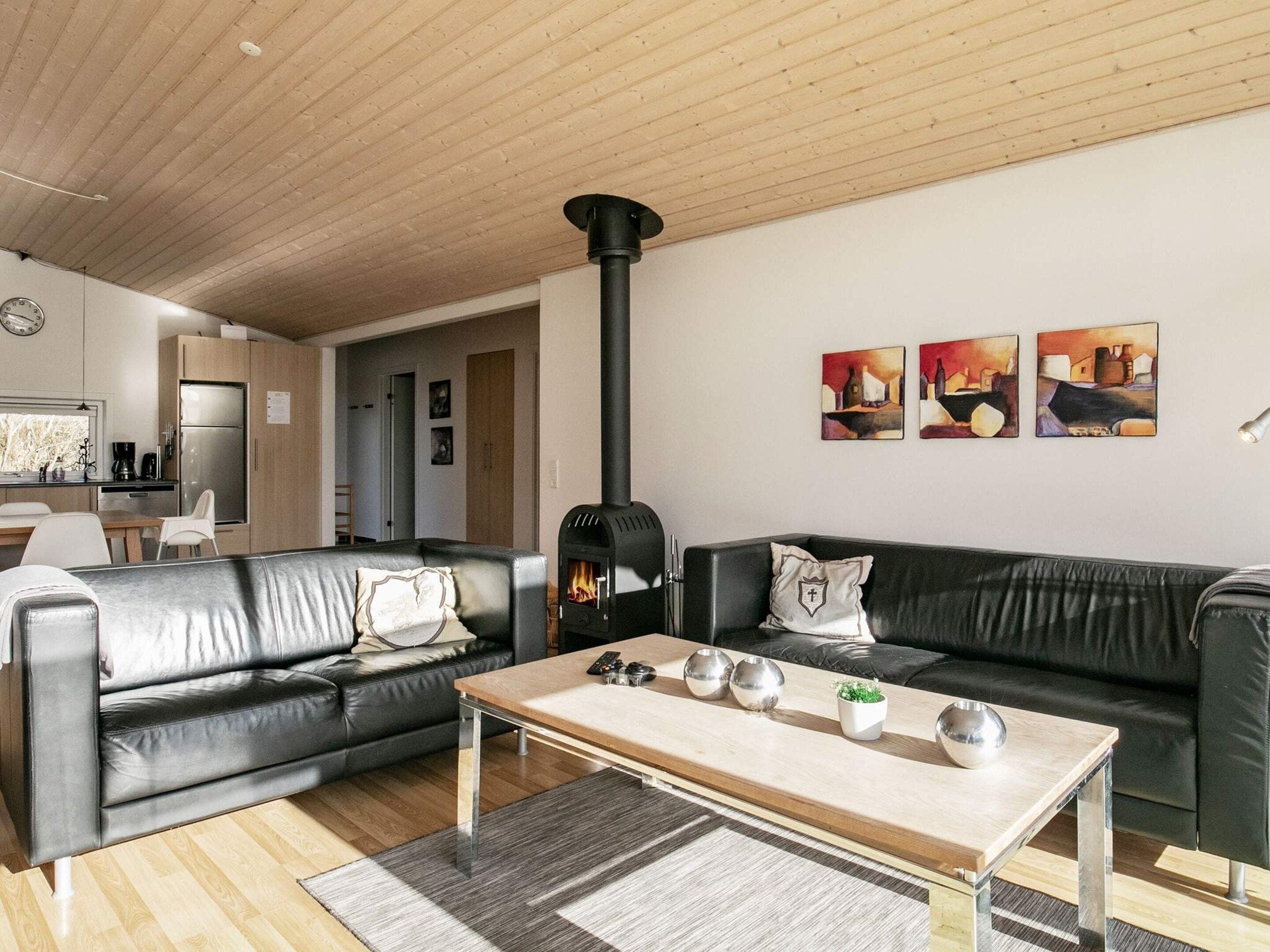 A modern living room with a black leather sofa, a wooden coffee table, and a black wood-burning stove.