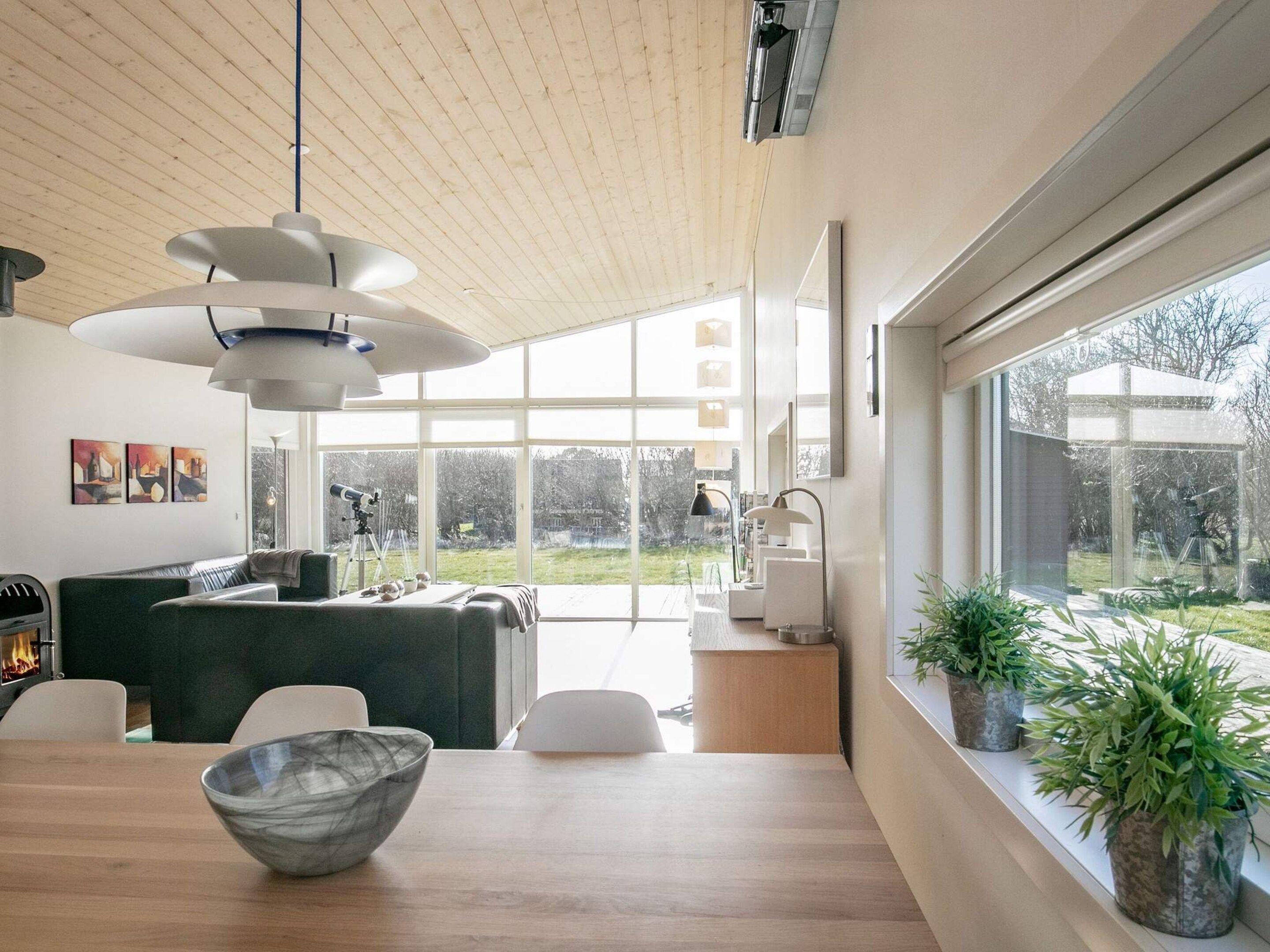 A modern living room with a wooden ceiling, large windows, a dining area with a bowl, and potted plants.