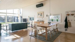 A modern kitchen with a wooden dining table, white chairs, and a large window providing a view of the outdoors.